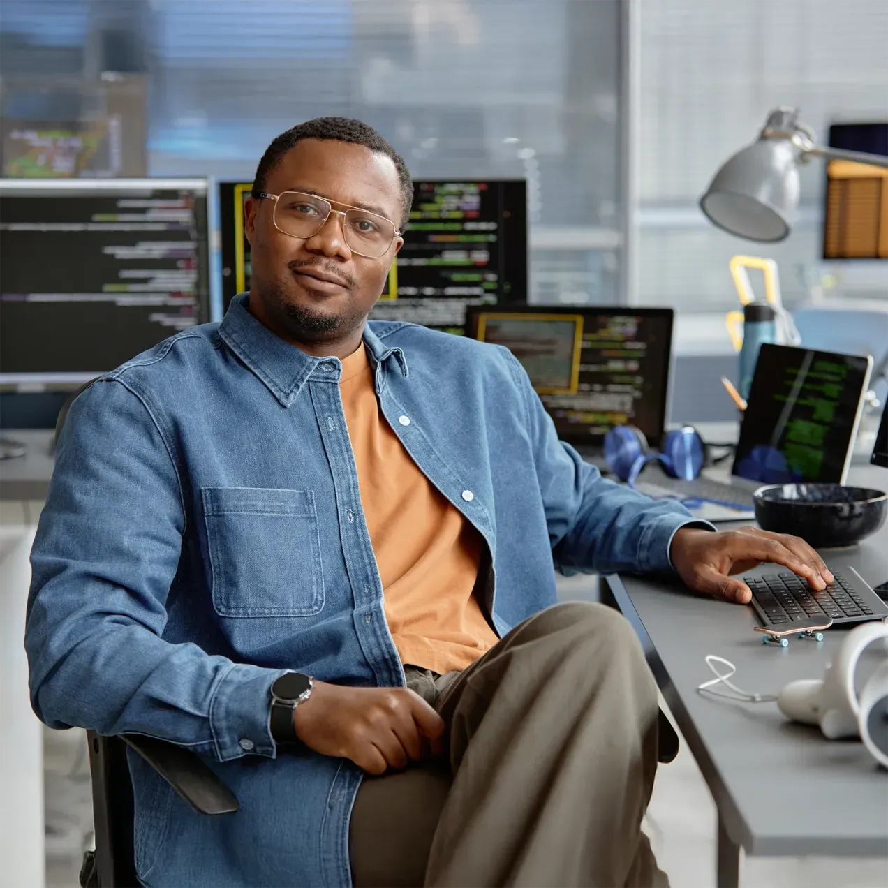 A confident cybersecurity professional sitting at a desk in a modern office, surrounded by multiple screens displaying lines of code, representing the expertise and practical skills gained through Herzing University’s graduate-level cybersecurity program.